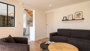 A modern living room with a grey sofa, a round wooden coffee table, and a bookshelf with framed pictures.