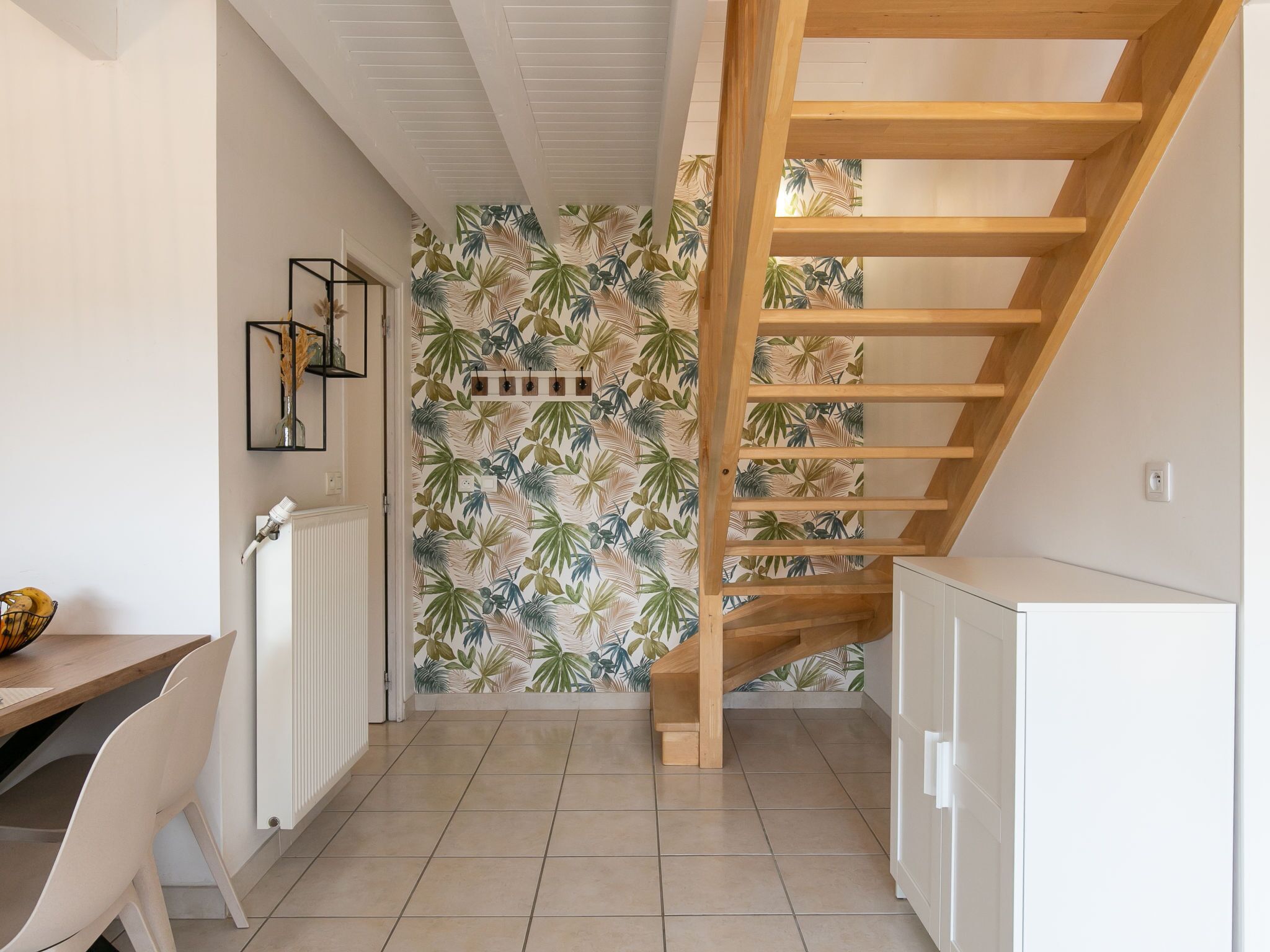 A kitchen with a wooden staircase, white cabinets, and a wall with a tropical leaf pattern.