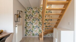 A kitchen with a wooden staircase, white cabinets, and a wall with a tropical leaf pattern. - La Roselière by Interhome (Guissény)