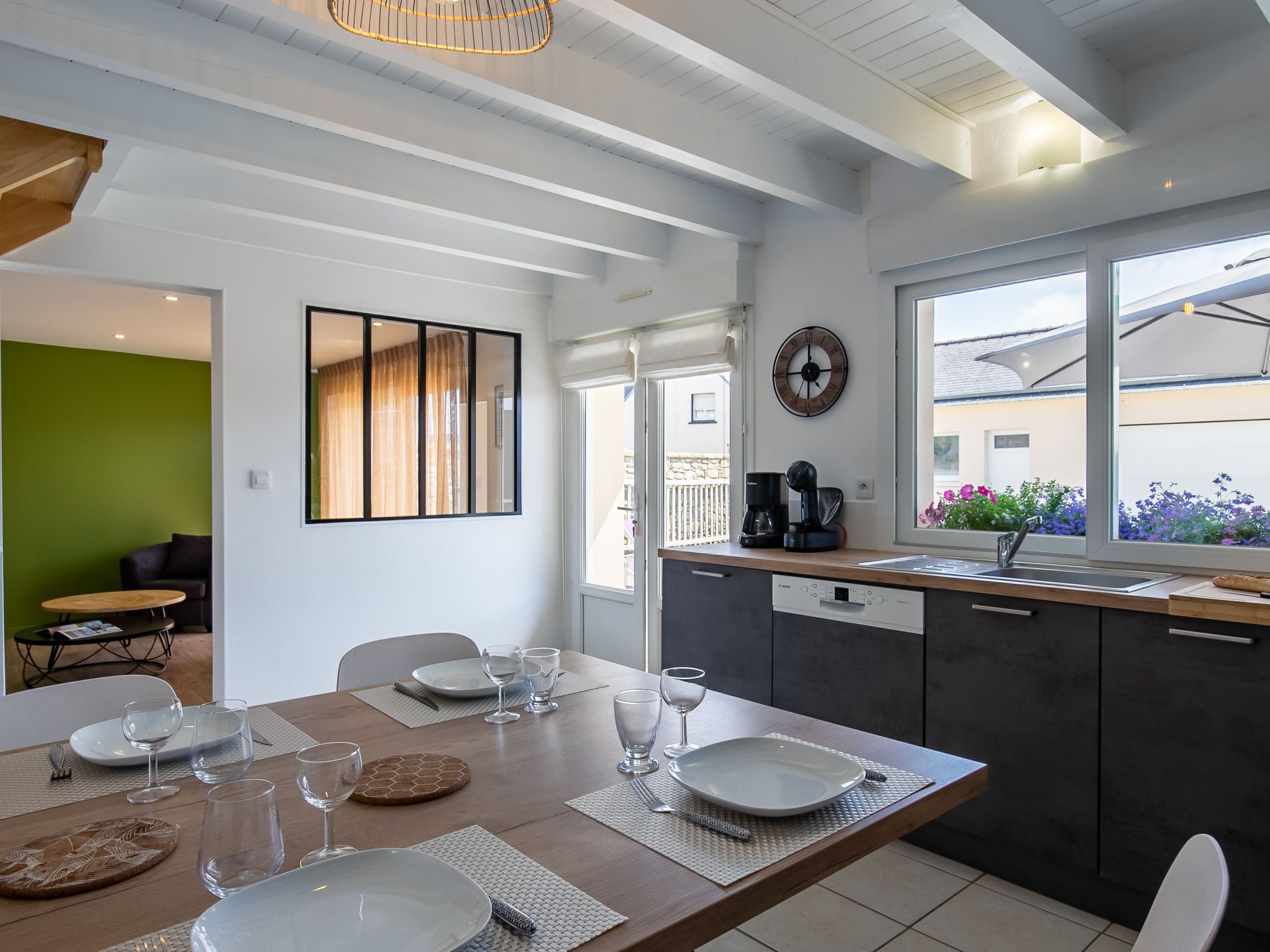 Een moderne keuken met een eethoek, met een houten tafel gedekt voor vier personen, een koffieapparaat en uitzicht op de omgeving.