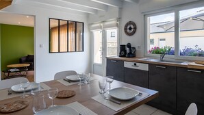 A modern kitchen with a dining area, featuring a wooden table set for four, a coffee machine, and a view of the outdoors. - La Roselière by Interhome (Guissény)