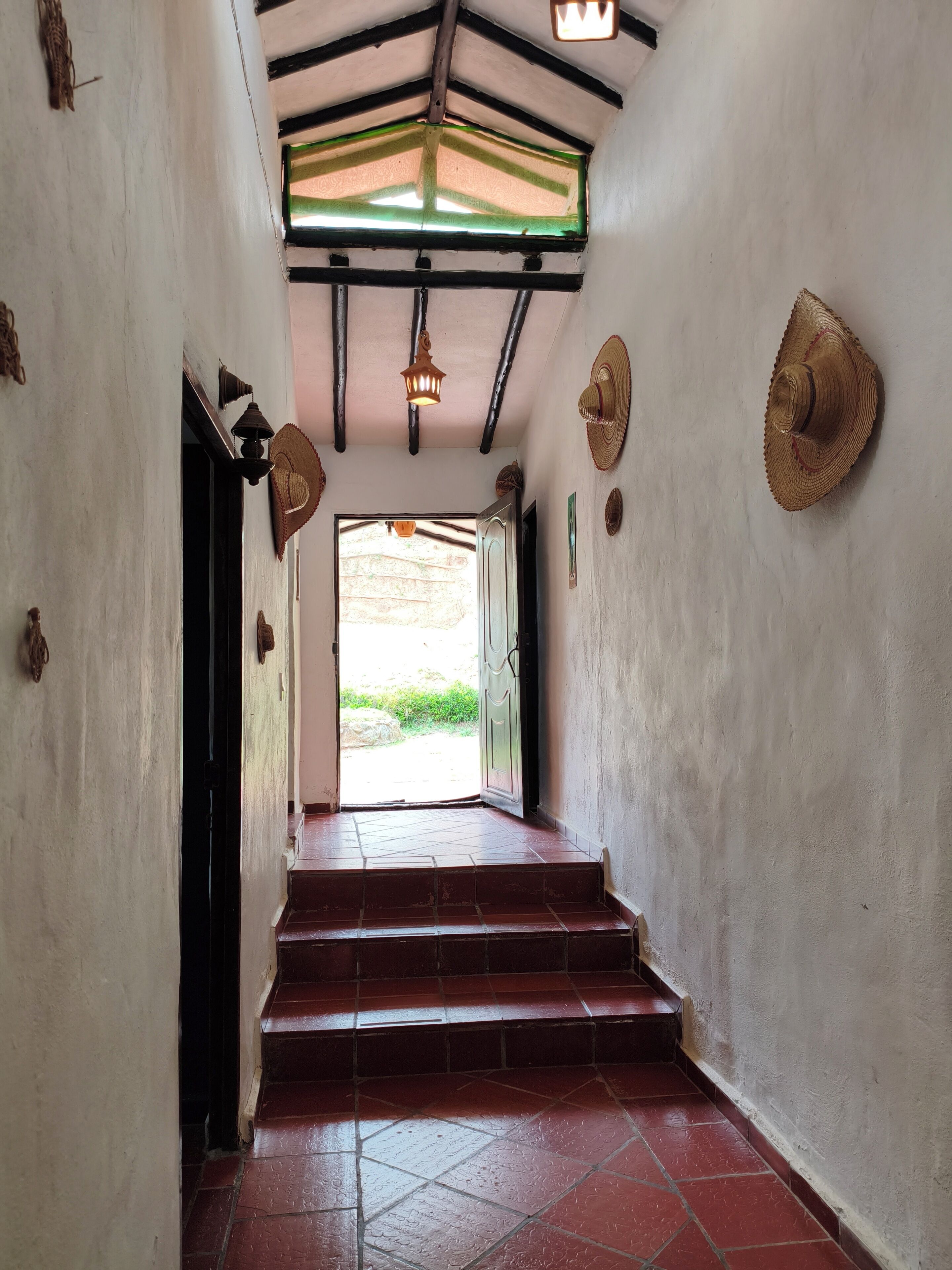 A hallway with a tiled floor leading to a door, a ceiling with exposed beams, and a hanging light fixture.