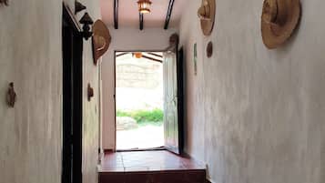A hallway with a tiled floor leading to a door, a ceiling with exposed beams, and a hanging light fixture.