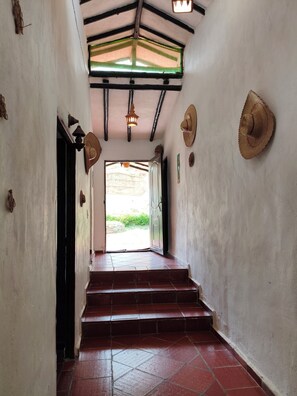 A hallway with a tiled floor leading to a door, a ceiling with exposed beams, and a hanging light fixture.