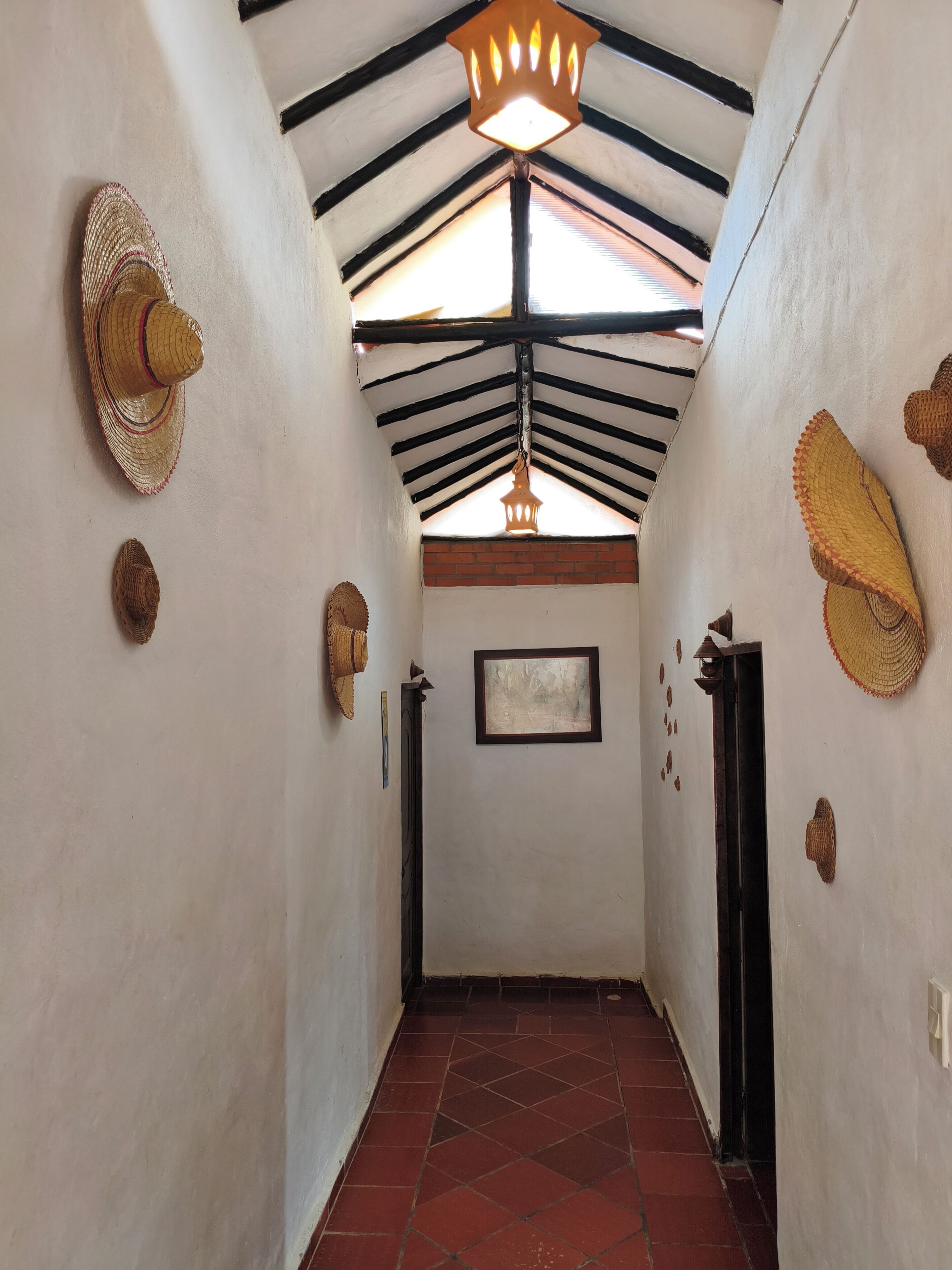 A hallway with a tiled floor, a ceiling with exposed beams, and wall-mounted hats.