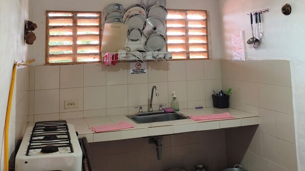 A kitchen with a gas stove, a sink, and a window with blinds. - Cabañas Cañón del Chicamocha (Aratoca)