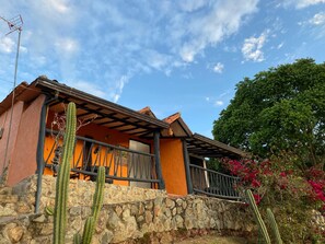 Un edificio con pared de piedra, terraza de madera y un cactus.