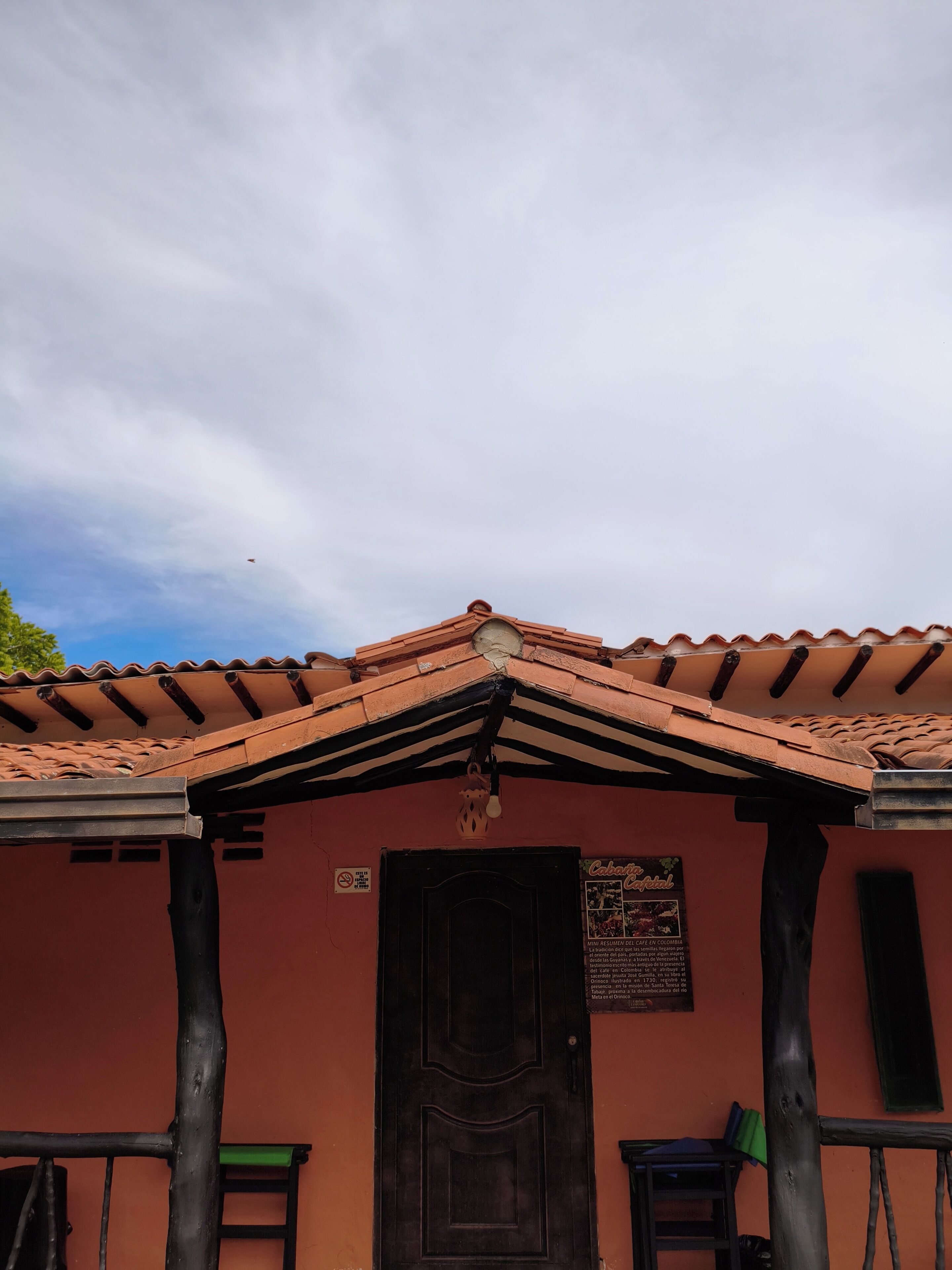 Un bâtiment avec un toit recouvert de tuiles, une porte sombre et une enseigne sur le mur.