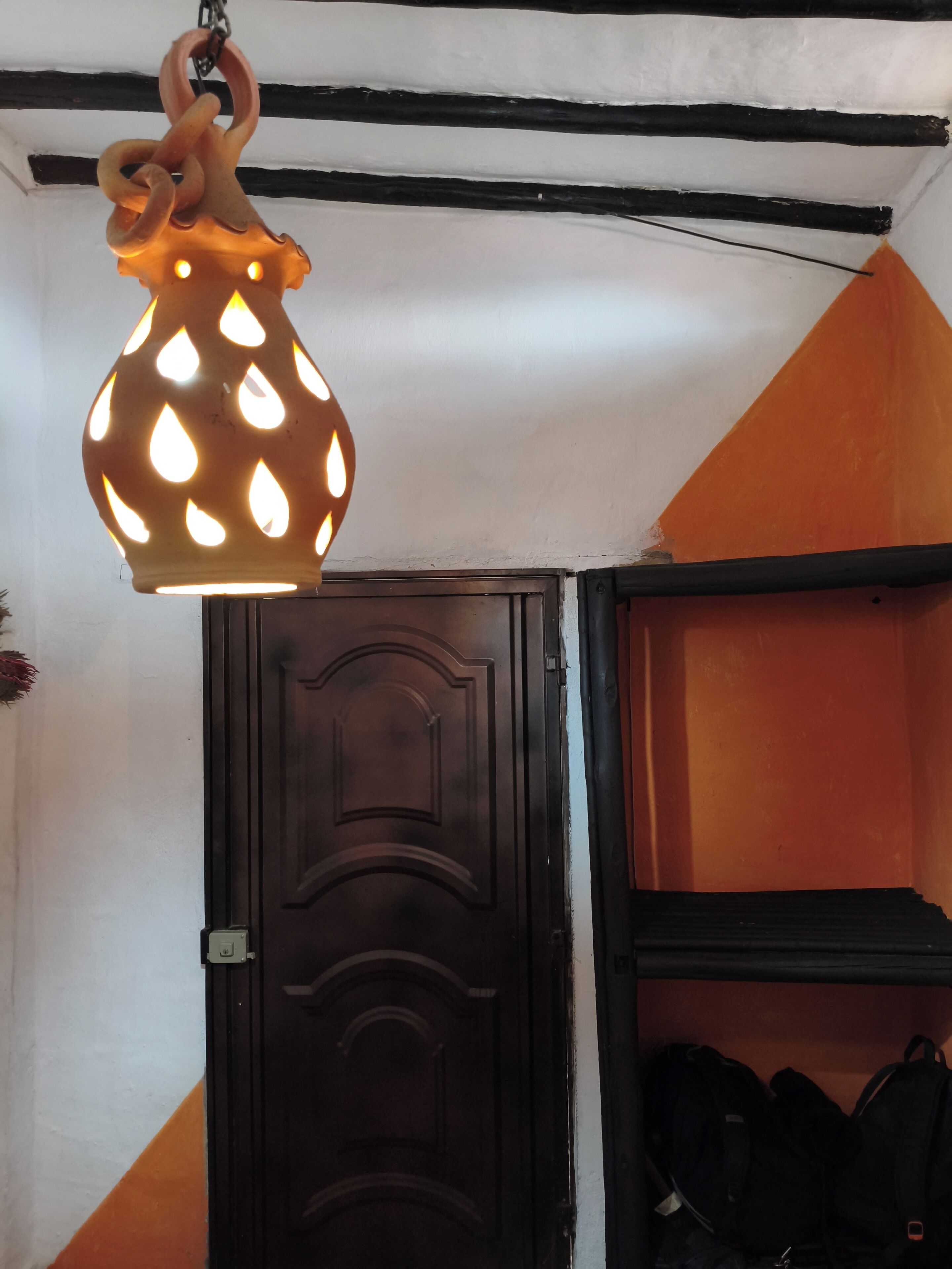 Una habitación con una puerta de madera oscura, una lámpara colgante con diseño de lágrima y una pared con motivo geométrico.