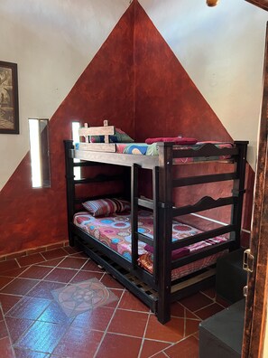 A bunk bed with a wooden frame and colorful bedding, positioned in a room with red walls and a tiled floor.