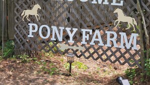 Een houten bord met de tekst 'WELCOME PONY FARM' en silhouetten van paarden.