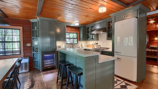 Eine moderne Küche mit Holzbalkendecke, einer integrierten Kücheninsel mit Hockern und einem großen Kühlschrank.