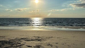 Une plage où l’on peut voir des empreintes de pas menant à l’eau, un ciel dégagé et le soleil se reflétant sur l’océan.