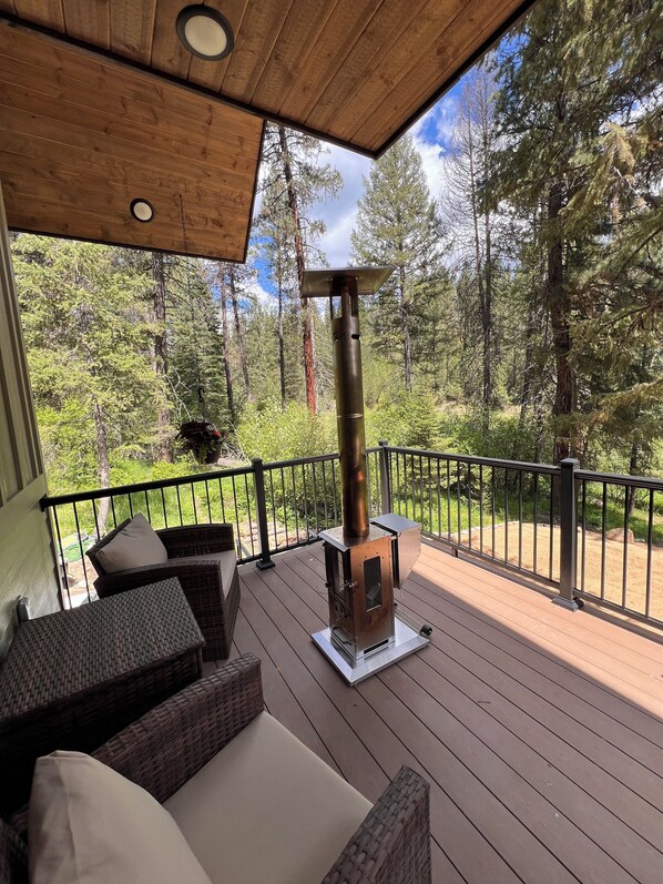 A wooden deck with a wood-burning stove, wicker furniture, and a view of a forest.