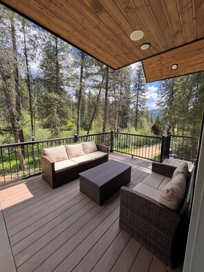 A covered deck with wicker furniture, a view of a forested area, and a hanging plant.