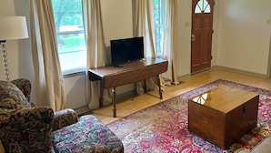 A living room with a TV on a wooden stand, a patterned sofa, a wooden coffee table, and a colorful rug.