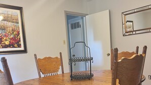 A dining room with a round wooden table, six wooden chairs, a metal chair rail, a framed painting, and a door.