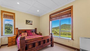 Een slaapkamer met een houten bed, een nachtkastje, een dressoir en een groot raam met uitzicht op een groen landschap.