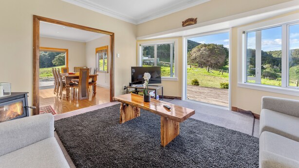Een ruime woonkamer met een open haard, een grote houten salontafel en een televisie. Er is een eethoek met een tafel en stoelen, en grote ramen met uitzicht op de omgeving.