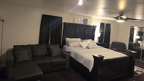 A bedroom with a bed, a sofa, a chair, a ceiling fan, and a lamp.