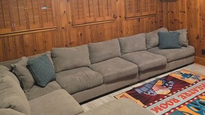 A living room with a sectional sofa, wooden panel walls, and a colorful rug.