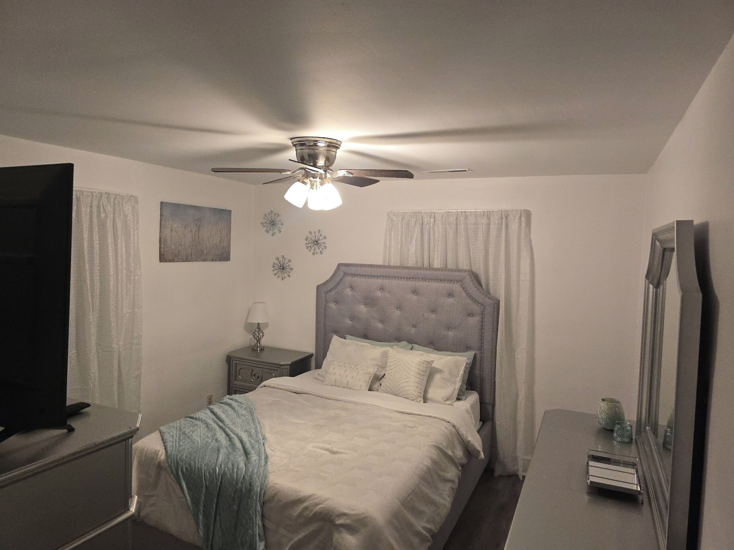 Un dormitorio con una cama, una mesita de noche, un aparador, un ventilador de techo y un espejo.