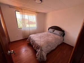 A bedroom with a bed, a window with curtains, and a wooden floor.