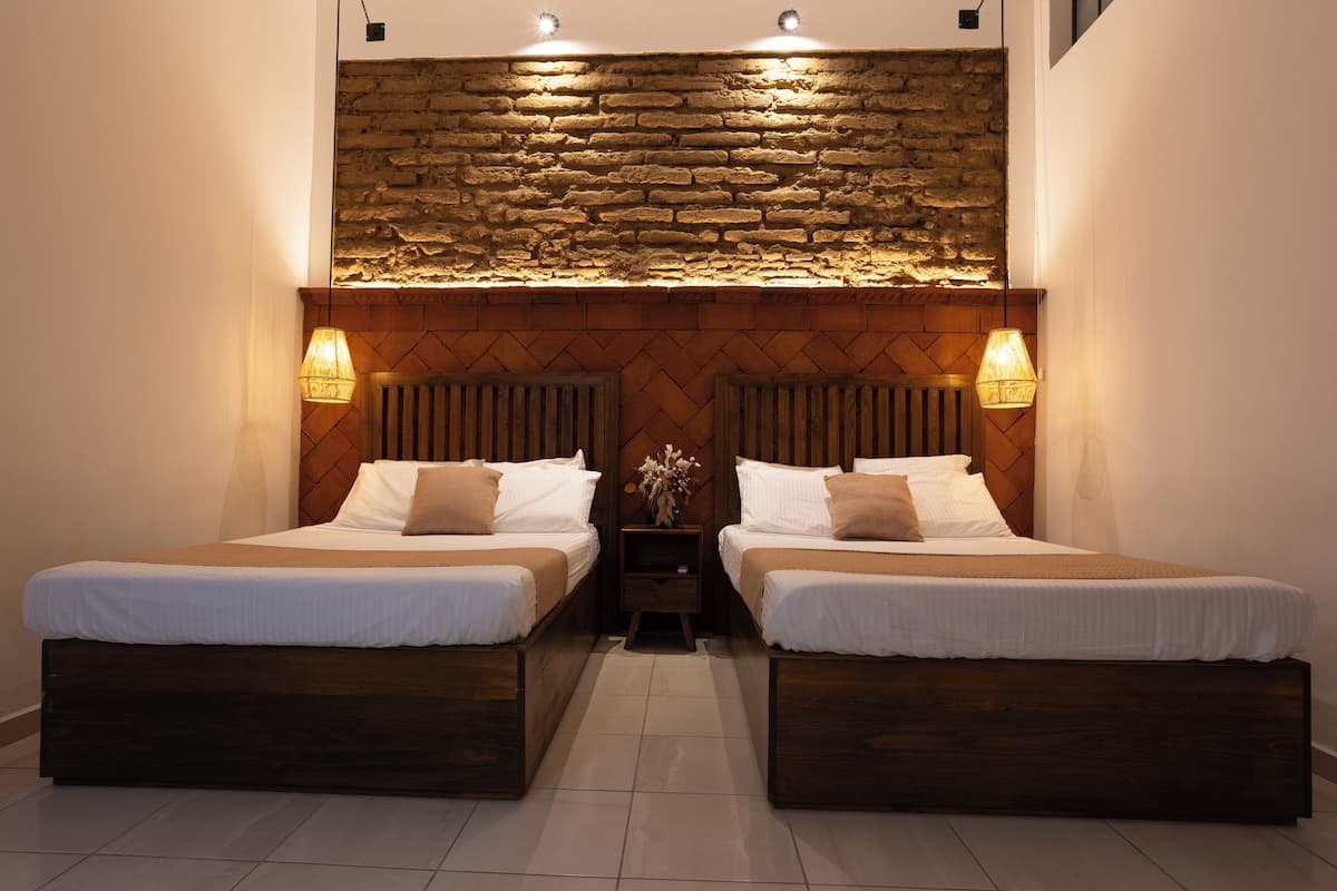 Quarto duplo com duas camas, uma parede de pedra e duas luminárias de cabeceira.