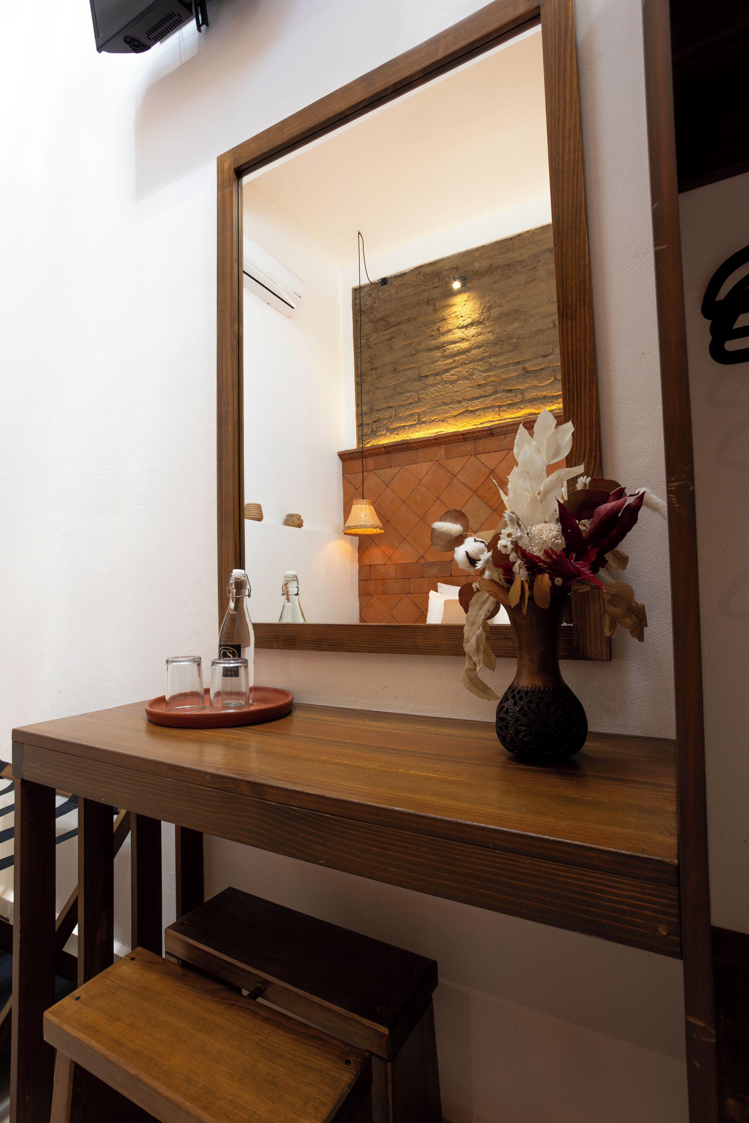A wooden vanity with a mirror, a vase with flowers, and a bottle on a tray.