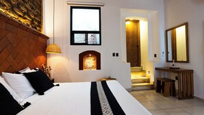 A hotel room with a large bed, a wooden headboard, a small window, a fireplace, a bathroom with a mirror, and a staircase leading to an upper floor. - Casa Sofi Oaxaca (Oaxaca)
