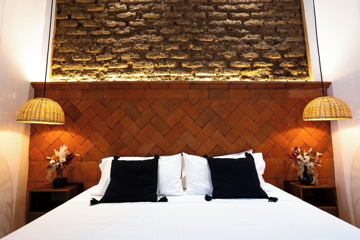 Uma cama bem arrumada com roupa de cama branca e preta, com duas mesas de cabeceira com luminárias e vasos de flores.