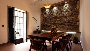A dining area with a large wooden table, several chairs, a stone wall, and a hanging light fixture. - Casa Sofi Oaxaca (Oaxaca)