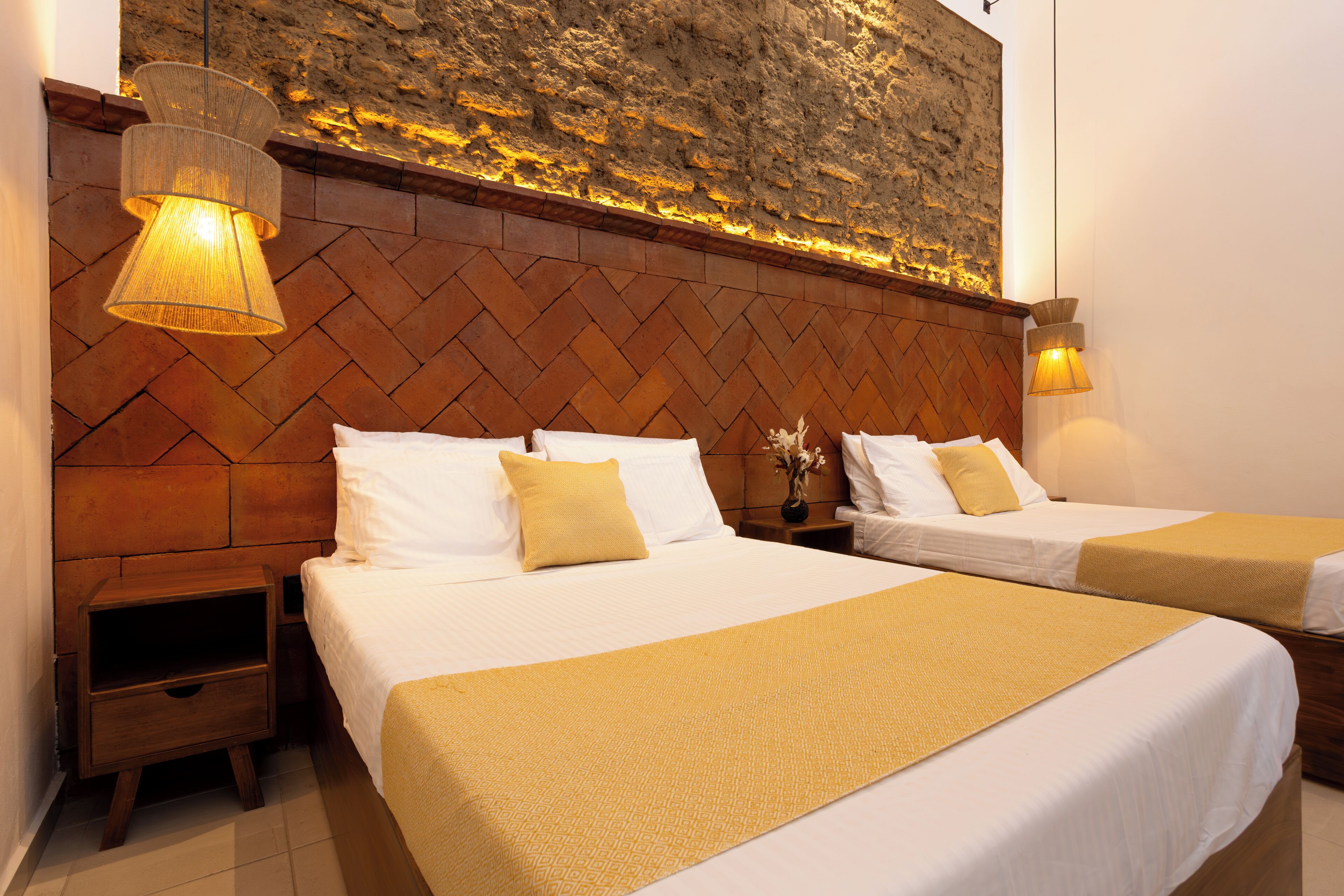 Una habitación de hotel con dos camas, cabecero de madera, mesitas de noche y lámparas fijadas a la pared.