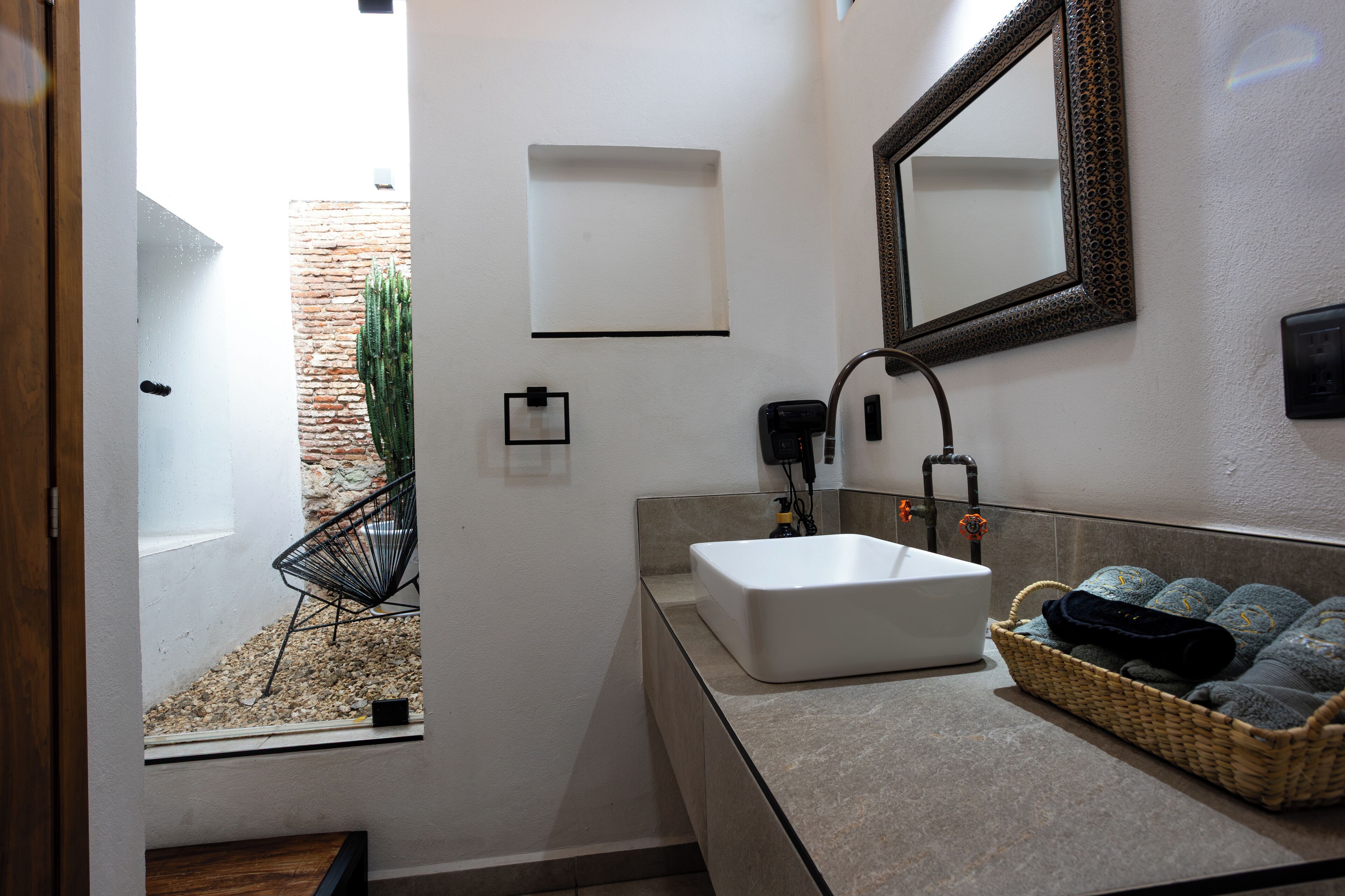 A modern bathroom with a large sink, a mirror, a small window, and a basket of towels.