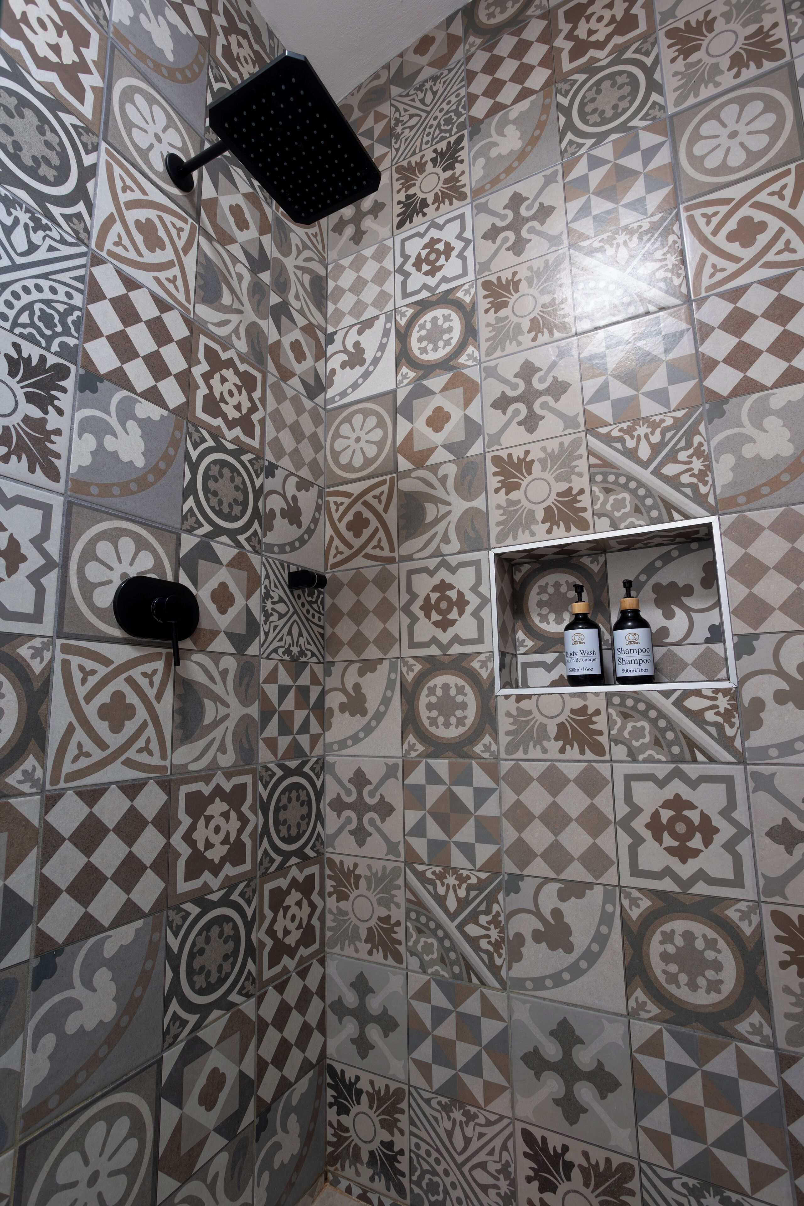 A bathroom with patterned tiles, a showerhead, and a shelf with two bottles of shampoo.