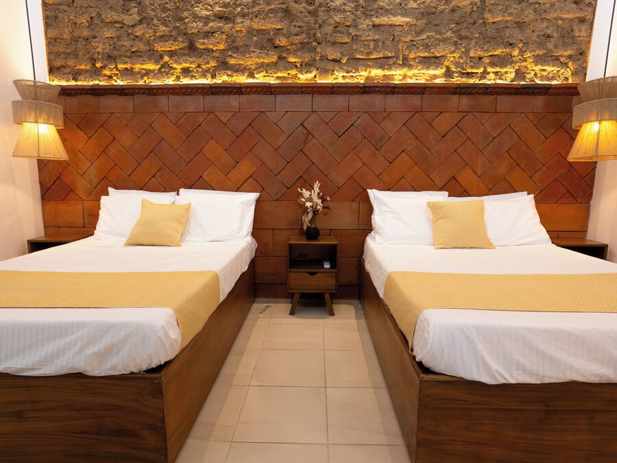 Camera d'albergo con due letti, una testiera in legno e un muro in pietra con illuminazione integrata.