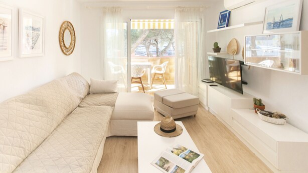A modern living room with a sofa, ottoman, flat-screen TV, and a dining area with chairs. - WELCS APARTAMENTO 165 PDA con piscina (Platja d´Aro)