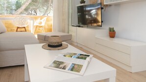 A modern living room with a white sofa, a coffee table with a magazine, a TV on a white cabinet, and a balcony with a chair. - WELCS APARTAMENTO 165 PDA con piscina (Platja d´Aro)