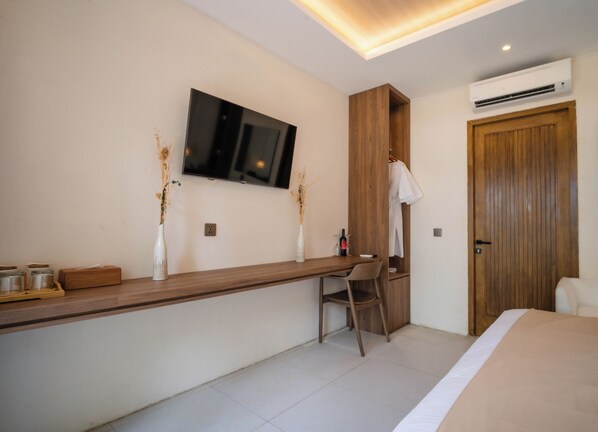 Une chambre d’hôtel moderne équipée d’un bureau en bois, d’un téléviseur à écran plat fixé au mur, d’une chaise, d’un lit et d’un appareil de climatisation.
