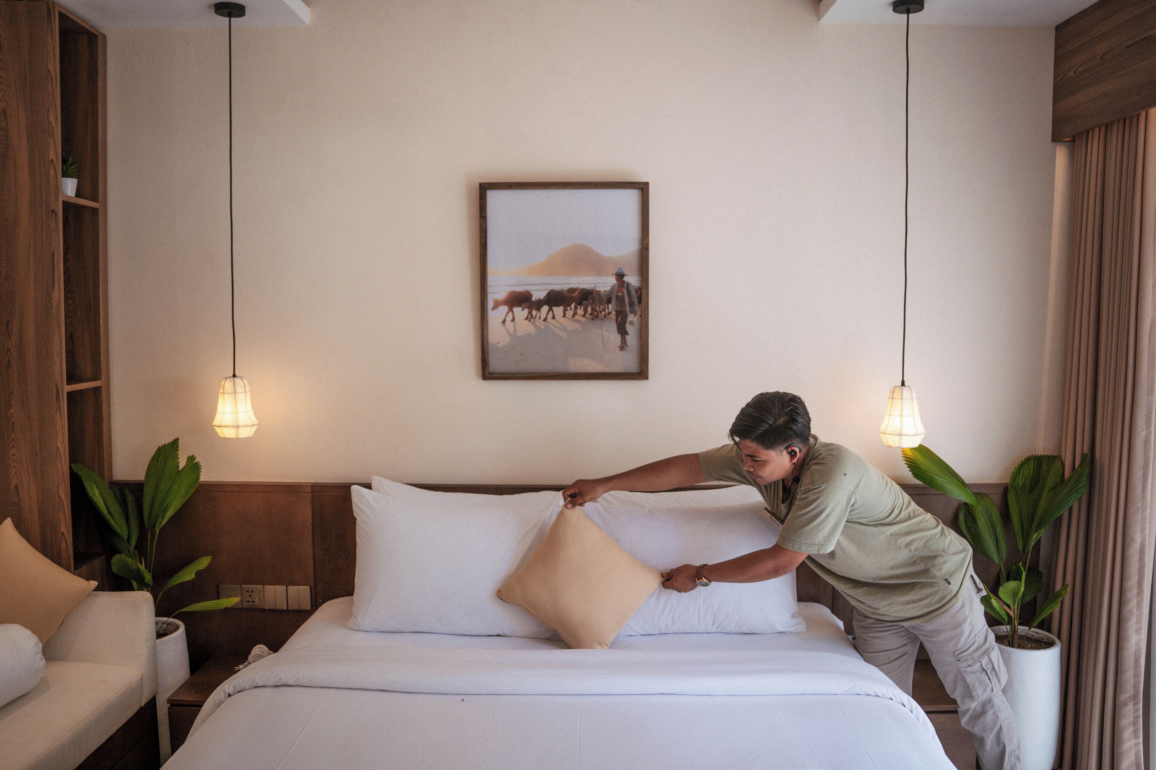 A neatly made bed with a single pillow, a wooden headboard, a framed picture on the wall, and two hanging pendant lights.