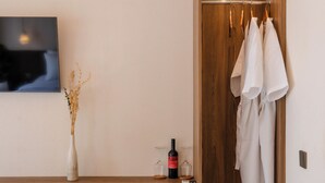 A modern room with a wooden desk, a chair, a TV mounted on the wall, a wooden wardrobe, and a small table with a bottle and glasses. - Tika Lombok (Kuta)