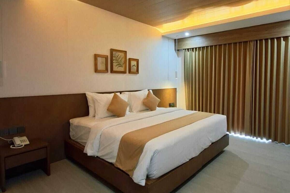 A hotel room with a large bed, a bedside table with a phone, and a window with curtains.