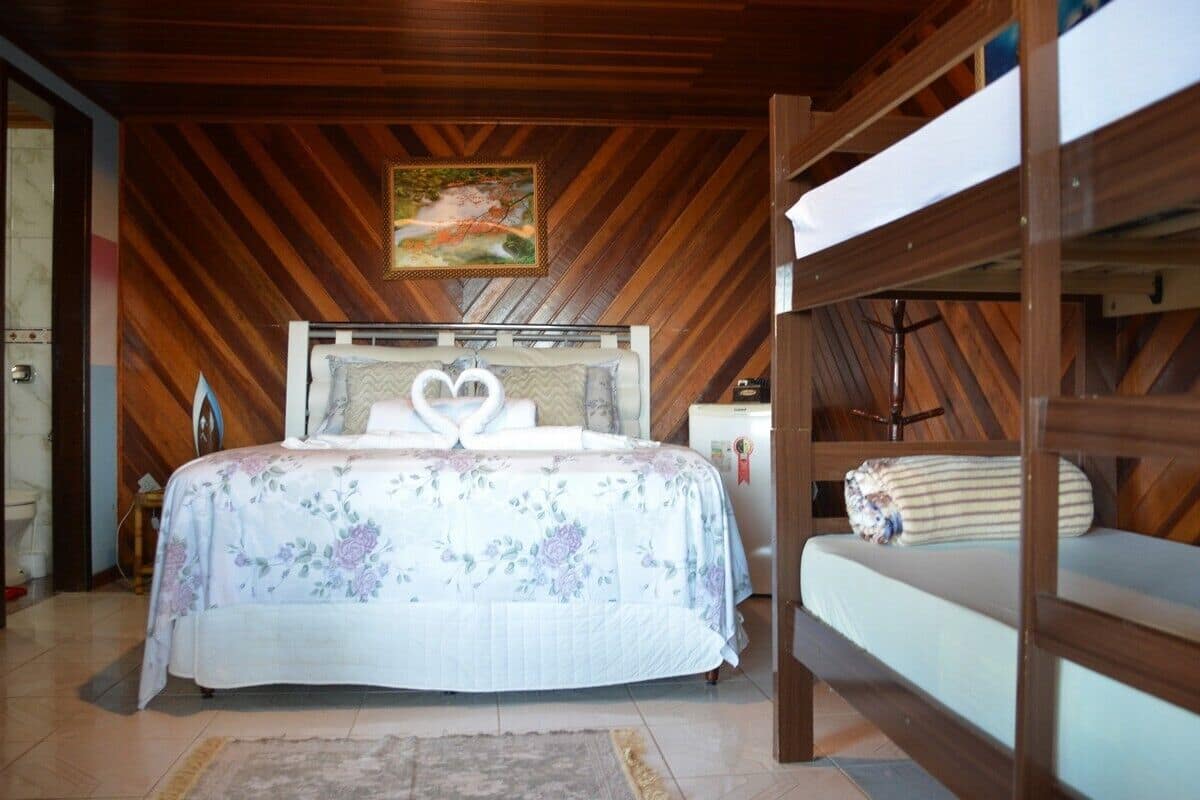 A bedroom with a wooden ceiling, a bed with floral bedding, a bunk bed, and a painting on the wall.