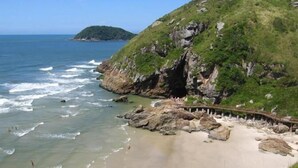 Una playa costera con acantilados rocosos, agua cristalina y una pasarela de madera.