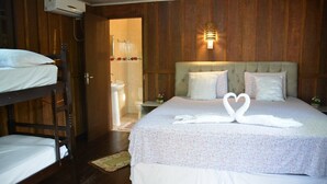 Una habitación de hotel con una cama litera, una cama individual con colcha estampada y un aplique de pared. Se ve un área de ducha a través de una puerta abierta.