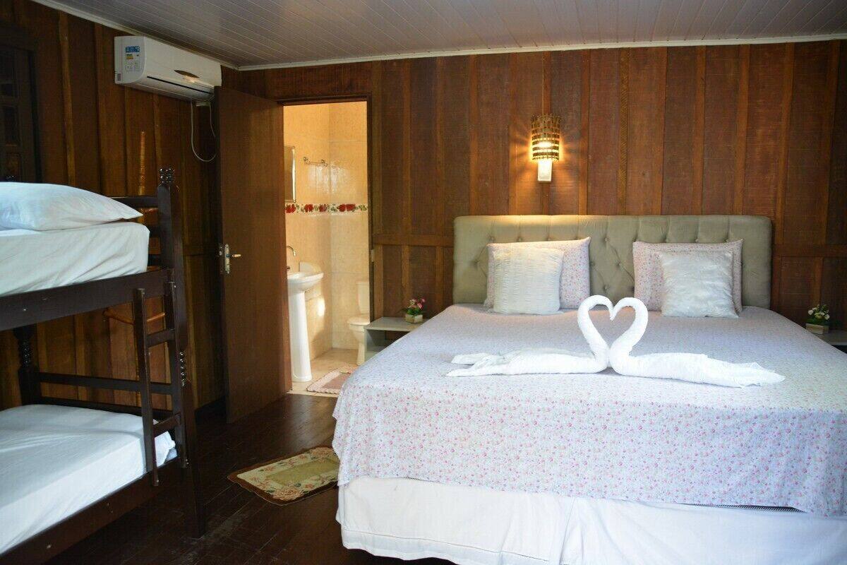 A hotel room with a bunk bed, a single bed with a floral bedspread, a wall-mounted light fixture, and a shower area visible through an open door.
