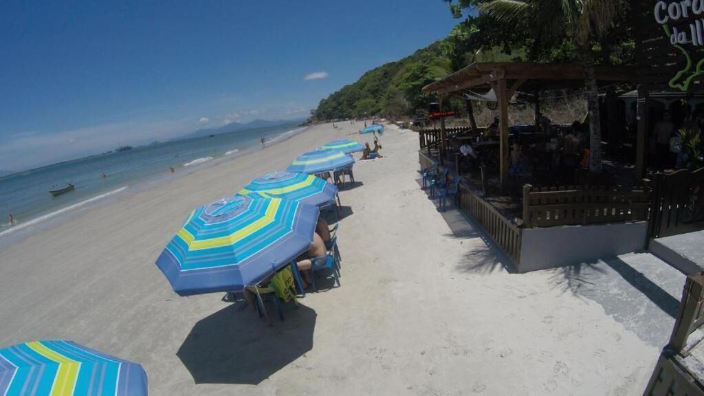 A beach with rows of striped umbrellas and beach chairs, a bar area with outdoor seating, and a view of the ocean.