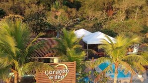 Un restaurante en la playa llamado 'Coração da Ilha', con terraza, piscina y palmeras.