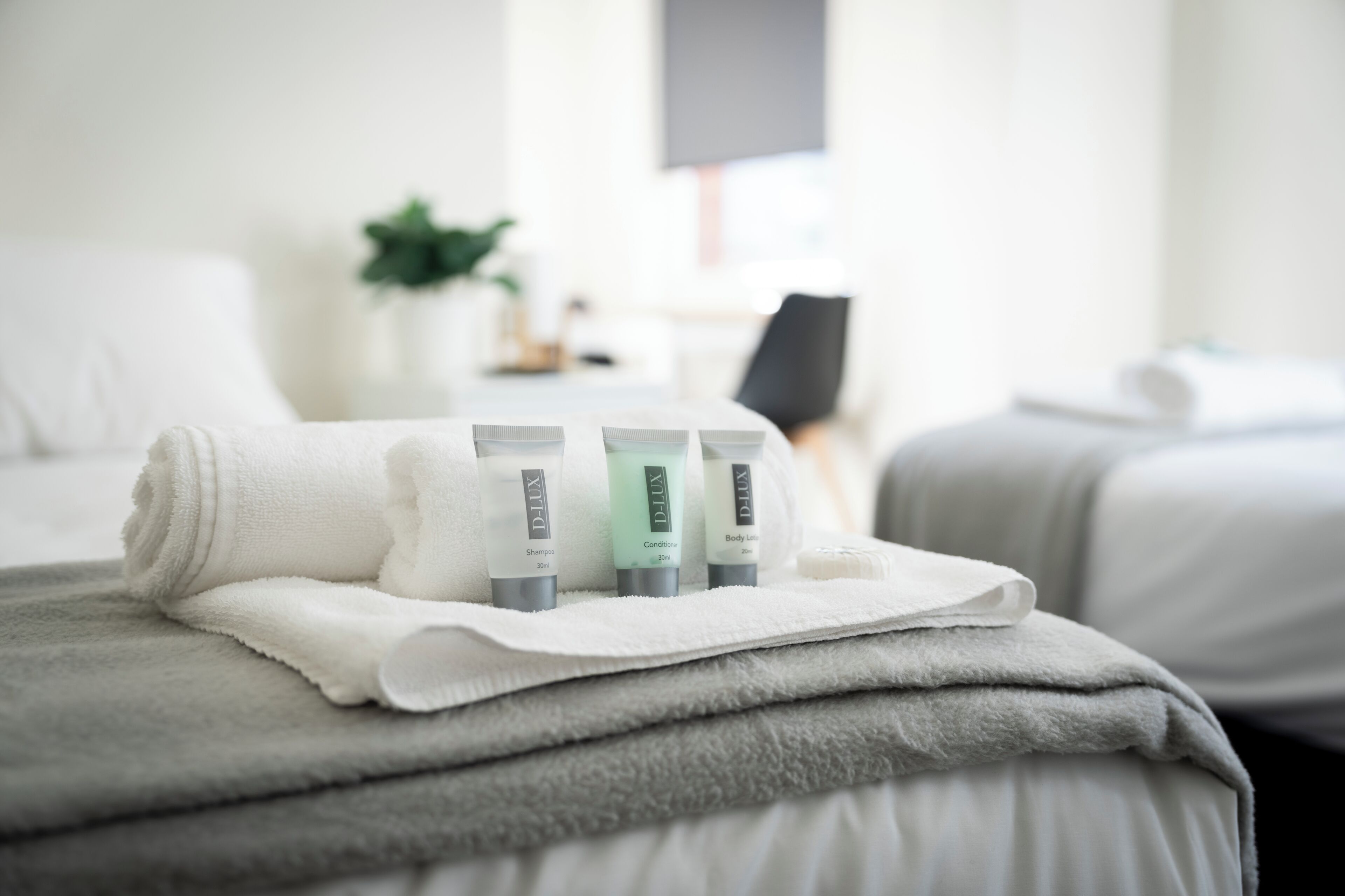 A neatly made bed with a white towel and three bottles of D-Lux products on top.