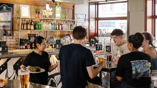 A bar with a variety of drinks and bottles, a counter with a menu, and a TV mounted on the wall. - Bar Broadway (Chippendale)